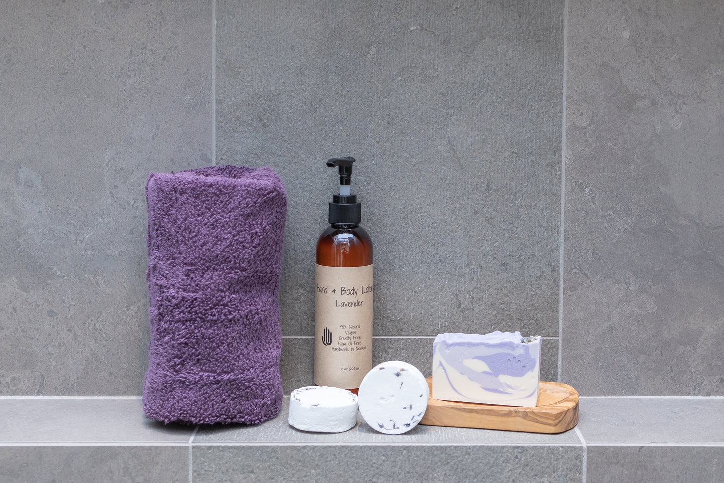 round wooden soap dish with a purple and white soap sitting on it placed on bathroom tiles with a towel shower steamers and lotion