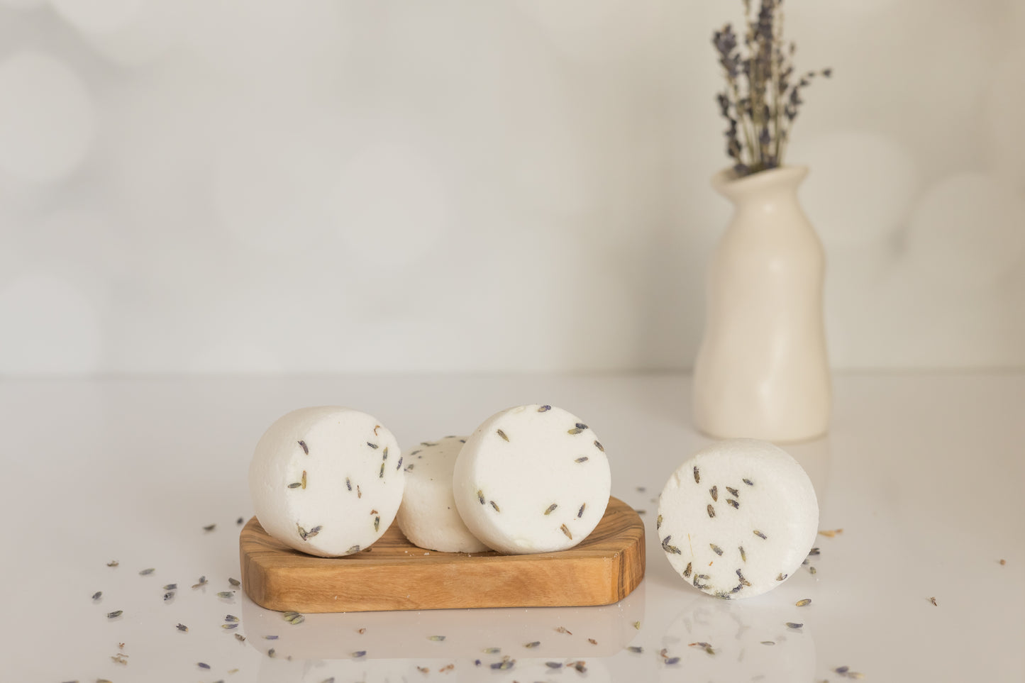 four peppermint shower steamers on a woden dish with a vase and lavender sprigs behind it